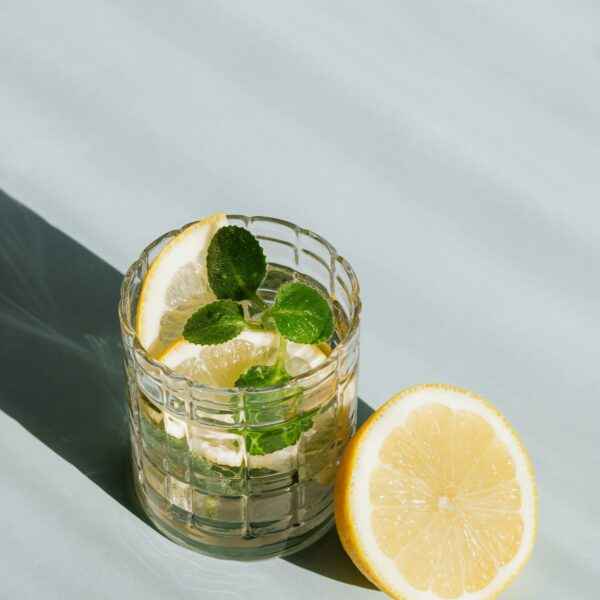Icy lemon mint drink in glass, half lemon beside, casting cool shadows on table.