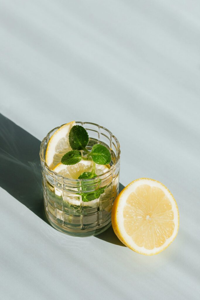 pexels-photo-4021887-4021887 Icy lemon mint drink in glass, half lemon beside, casting cool shadows on table.