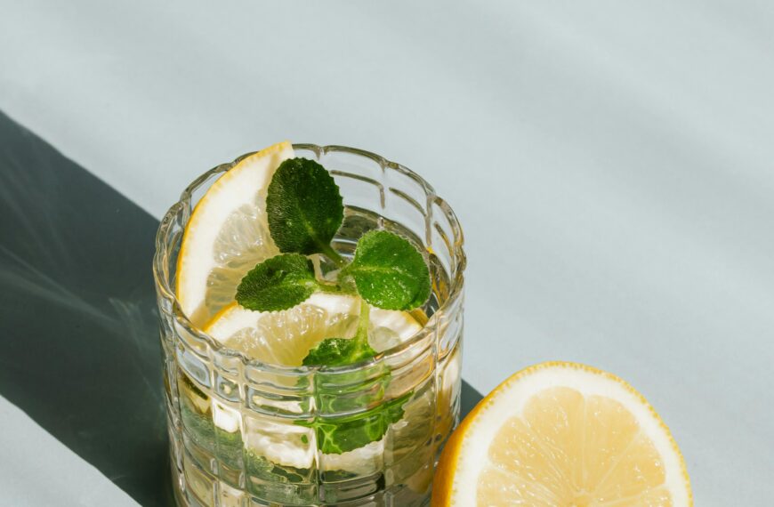 Icy lemon mint drink in glass, half lemon beside, casting cool shadows on table.