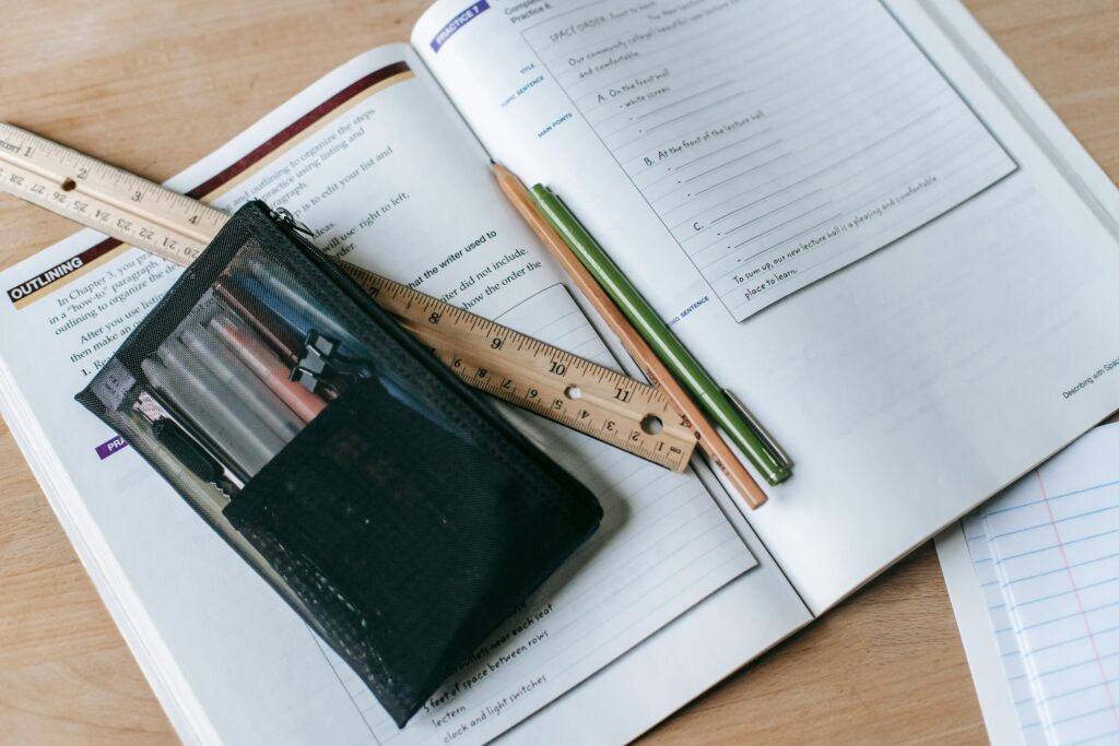pexels-photo-5905522-5905522 From above of textbook with exercises and ruler with pens near small case on table