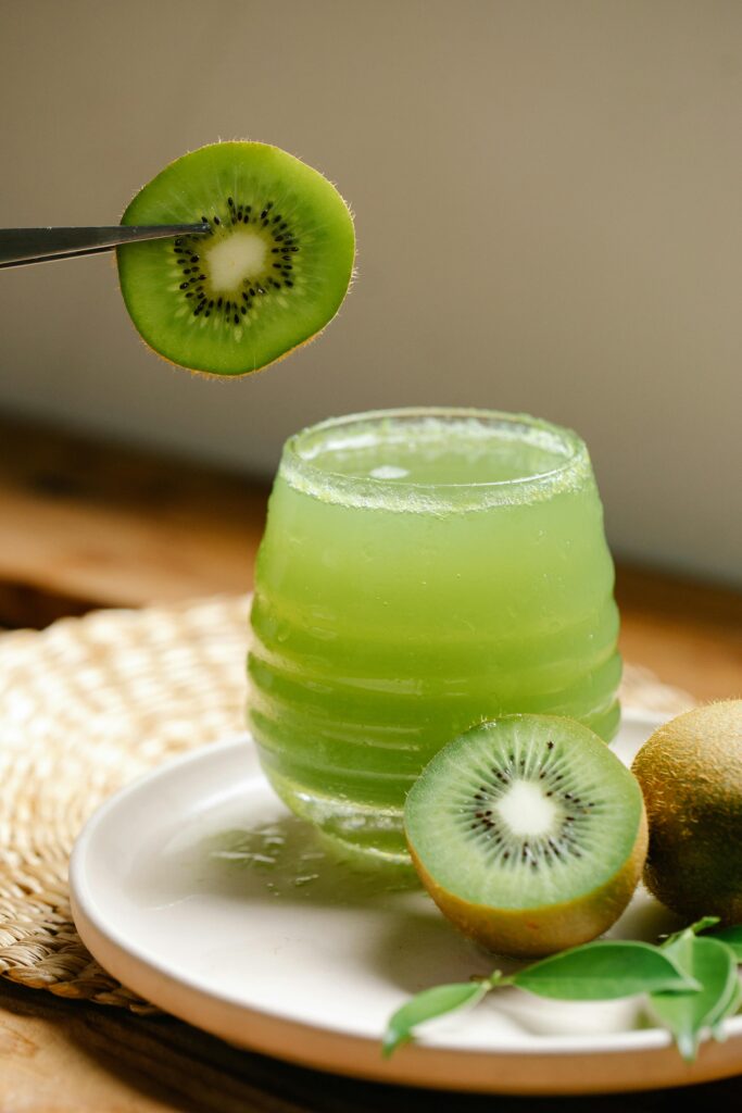 pexels-photo-8679385-8679385 Close-up of a glass filled with fresh kiwi juice and garnished with sliced kiwi on a plate.